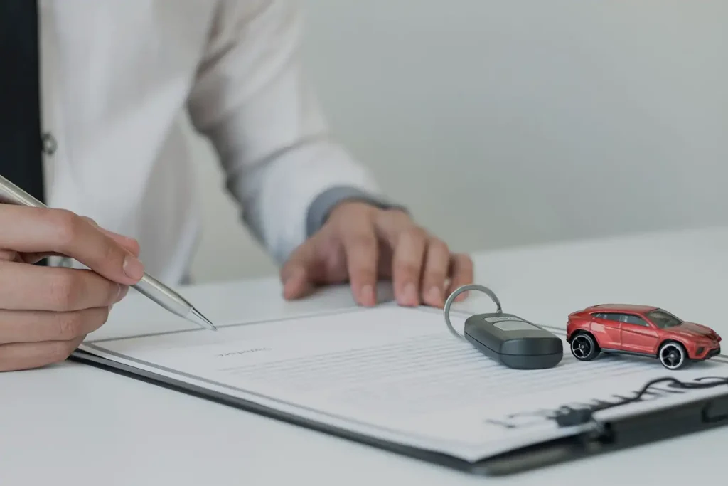 Signature d'un contrat d'assurance auto à côté d'une clé de voiture et d'une voiture miniature