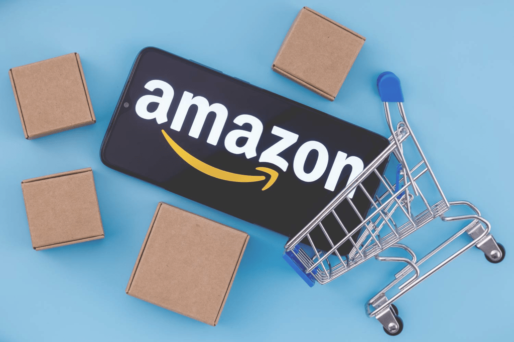 Smartphone avec logo Amazon à côté d'un mini chariot de shopping et des boîtes en carton