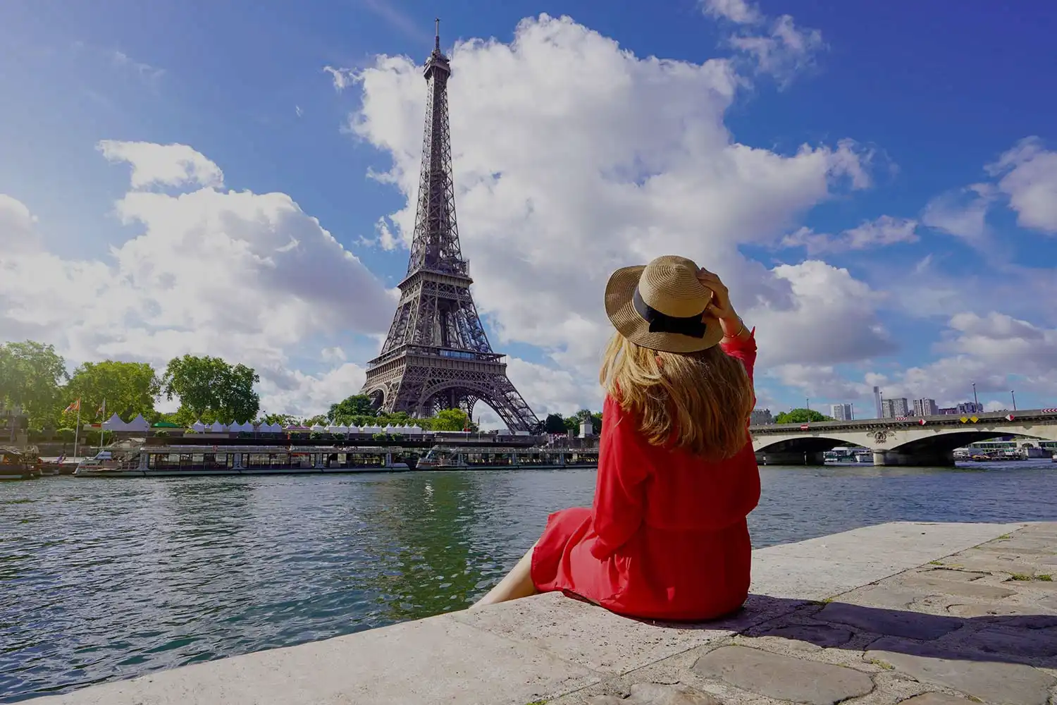 Une femme en robe rouge et chapeau de paille assise face à la Tour Eiffel à Paris, France