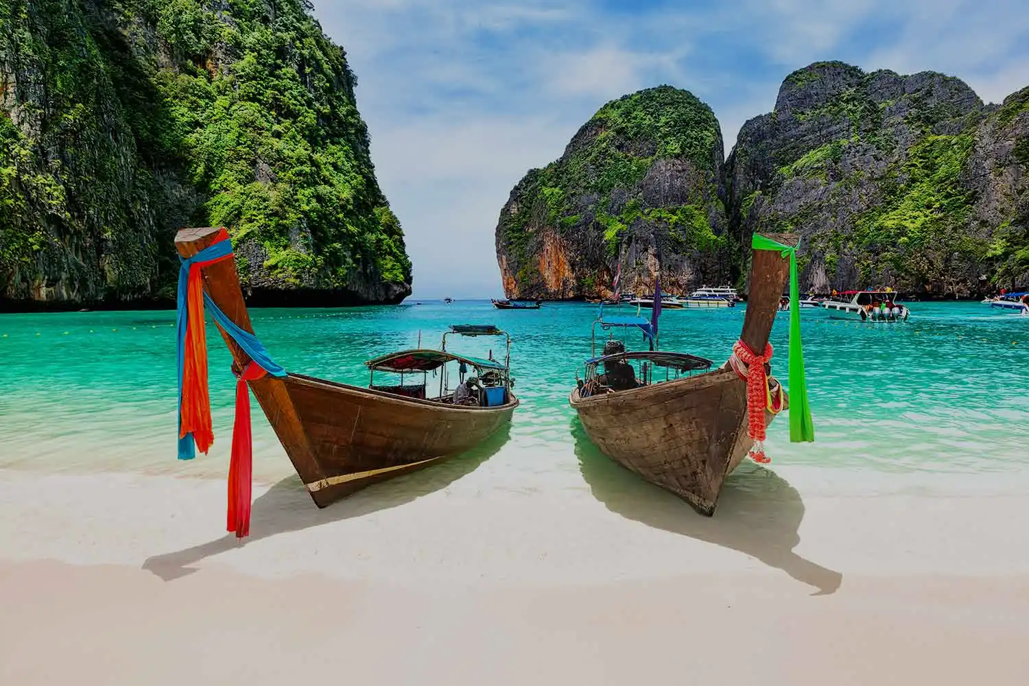 Deux bateaux traditionnels en bois sur une plage de sable blanc avec des eaux turquoises et des falaises verdoyantes en Thaïlande