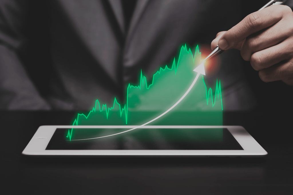Main dessinant une flèche ascendante sur une tablette affichant des graphiques boursiers verts