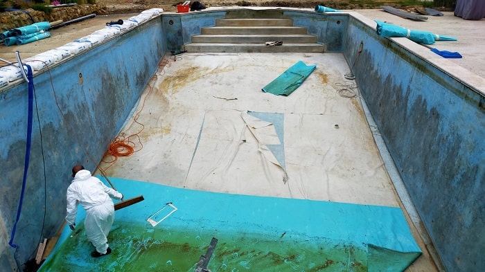 Piscine vide en cours de rénovation avec travailleur en combinaison.